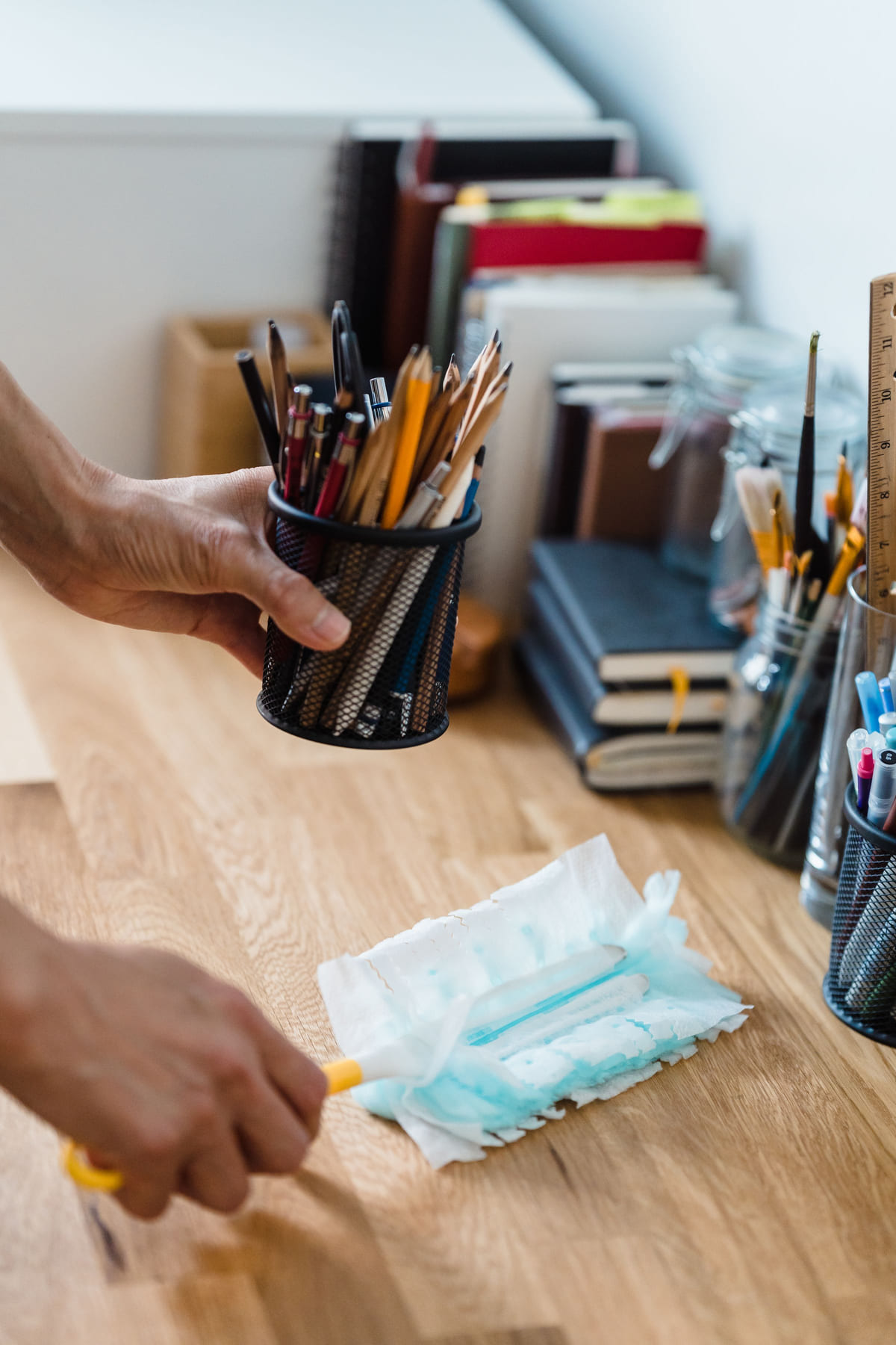 Gloved hands wiping a desk beside neatly arranged office supplies.
