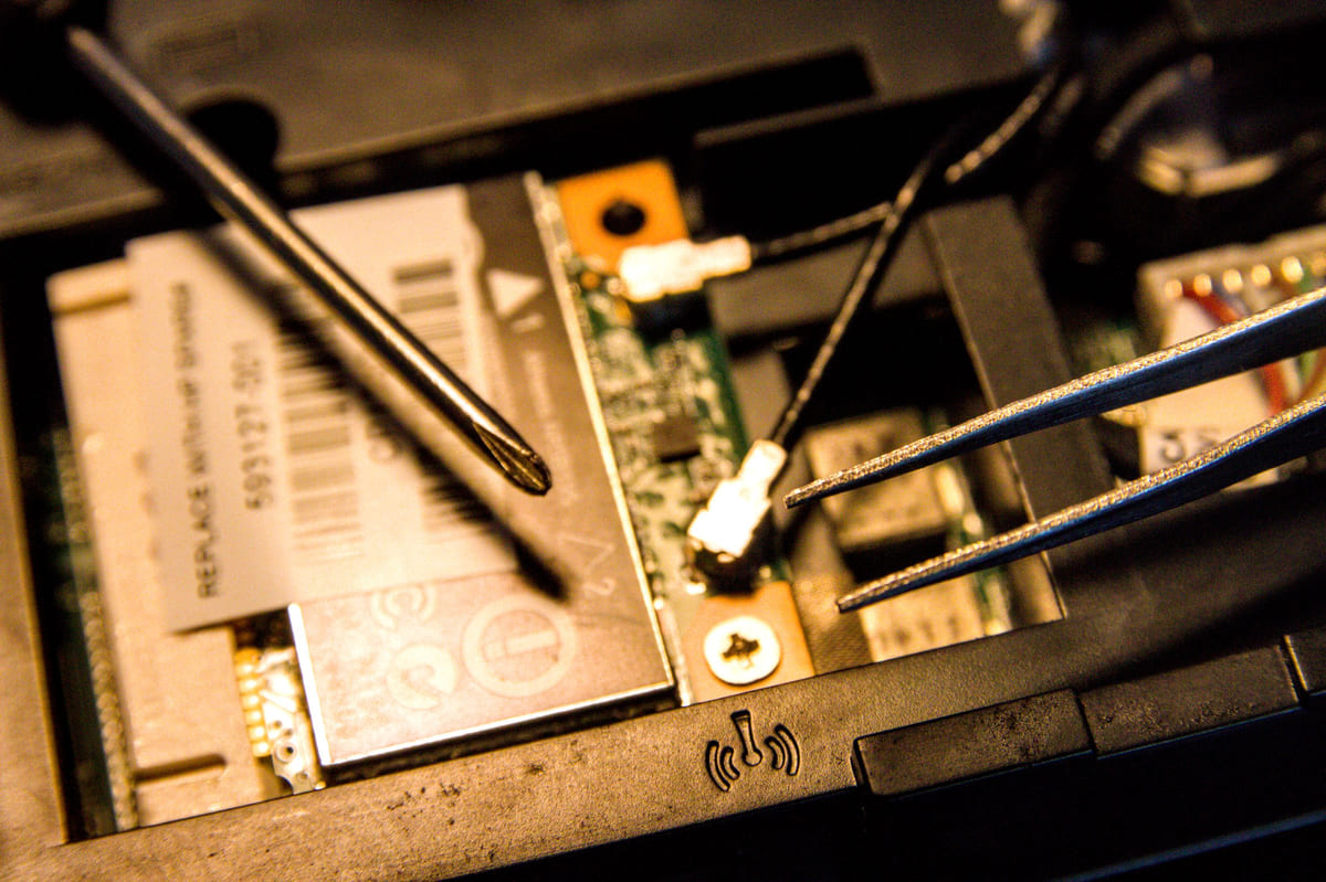 Small tools being used on an opened laptop's internal components.