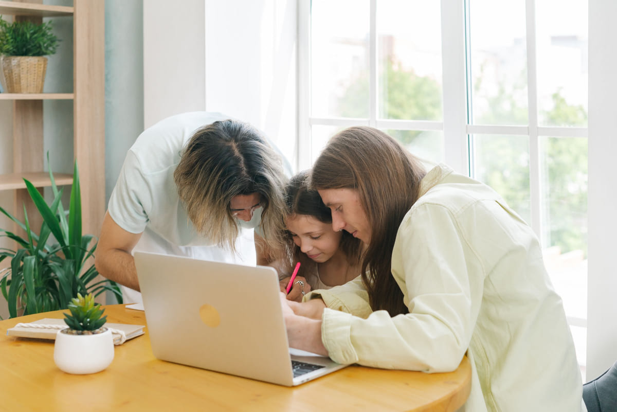 Parents helping their daughter with schoolwork at a bright table.