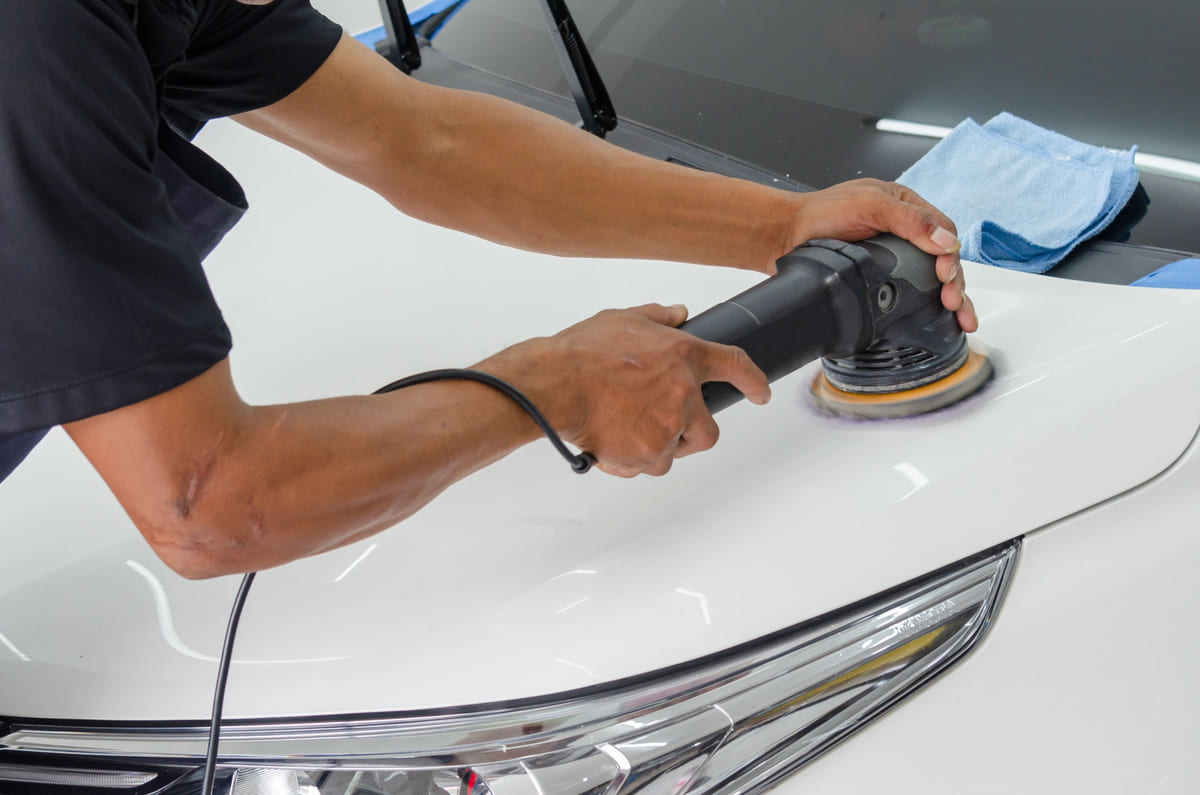 A person using a polishing machine on a white car's bodywork.