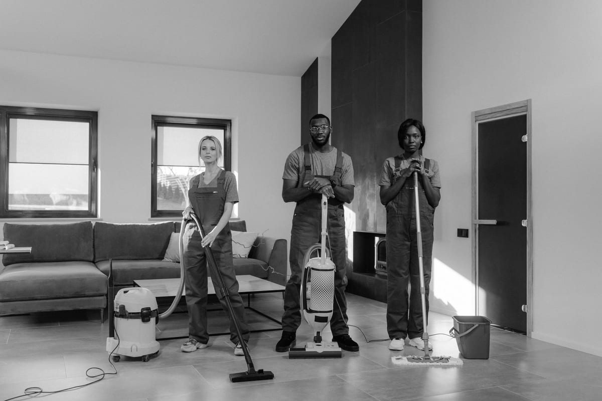 A cleaning team standing with vacuum cleaners and cleaning supplies in a living room.