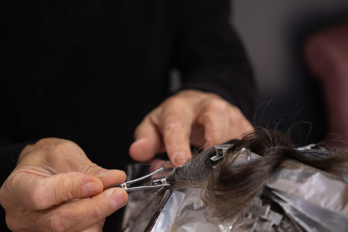 A close-up of a stylist working on foil-wrapped sections of hair.