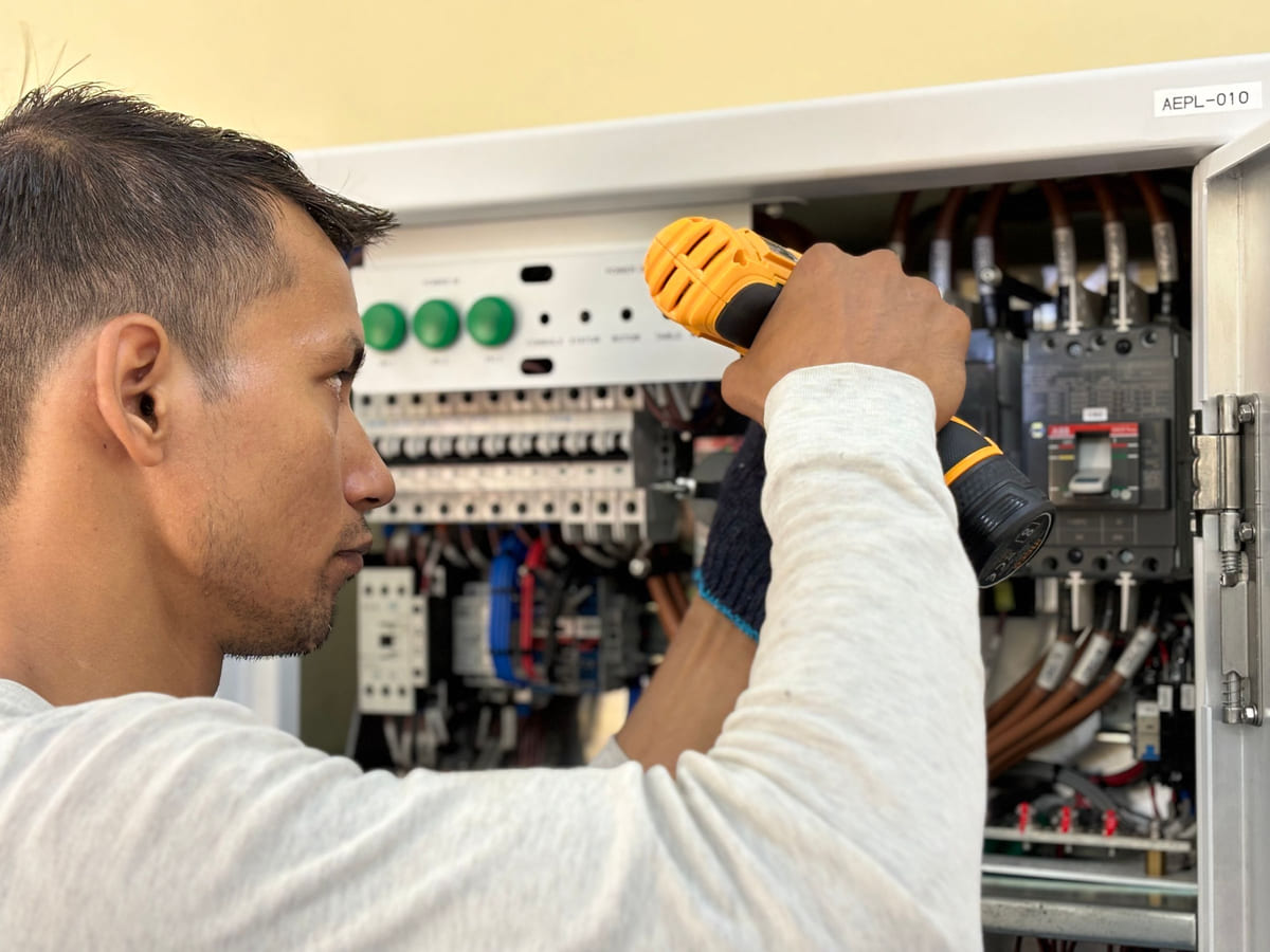 An electrician working inside an open electrical control panel.
