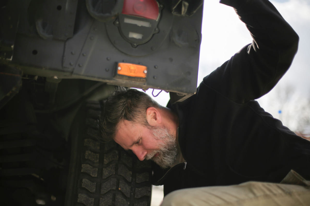 A mechanic inspecting a wheel area beneath a raised car.