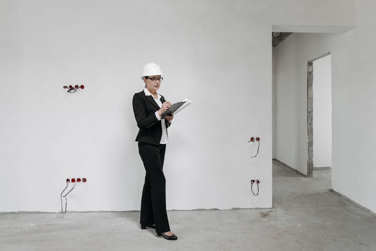 A professional in a hard hat assessing a room with a clipboard.