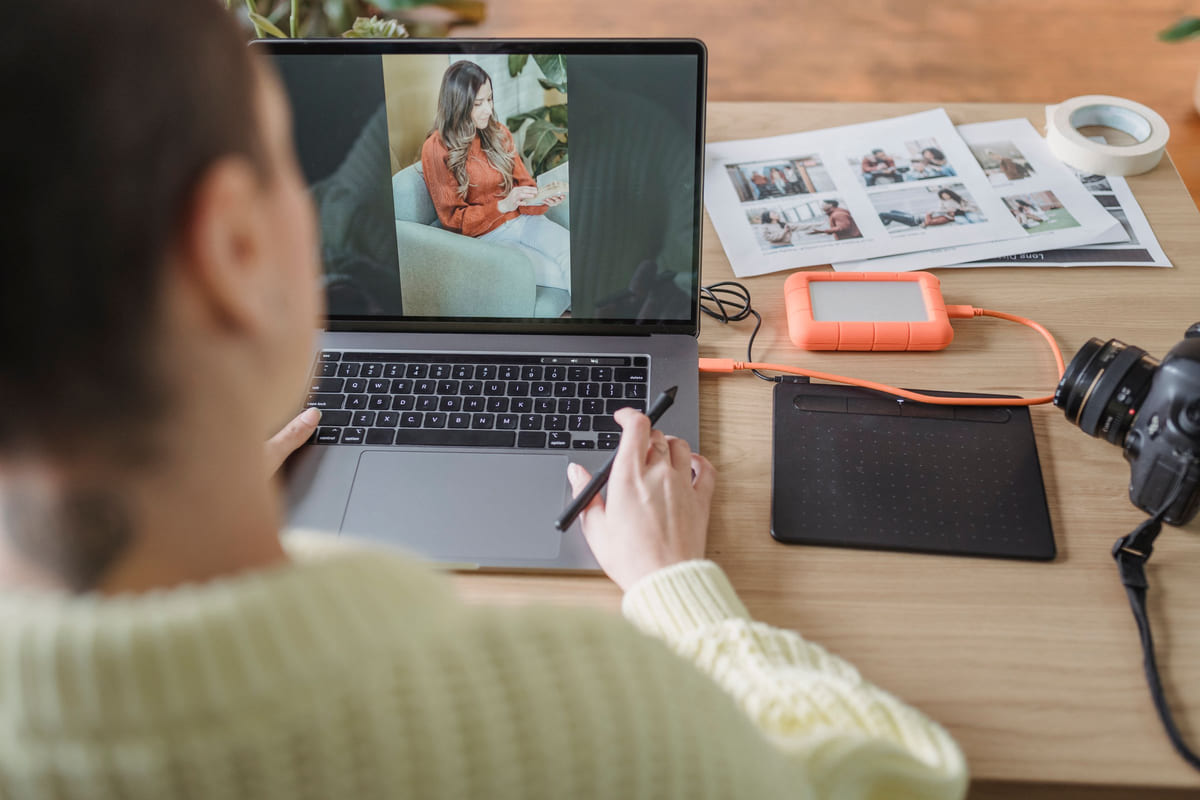 A person editing a portrait on a laptop beside a camera and printed photographs.