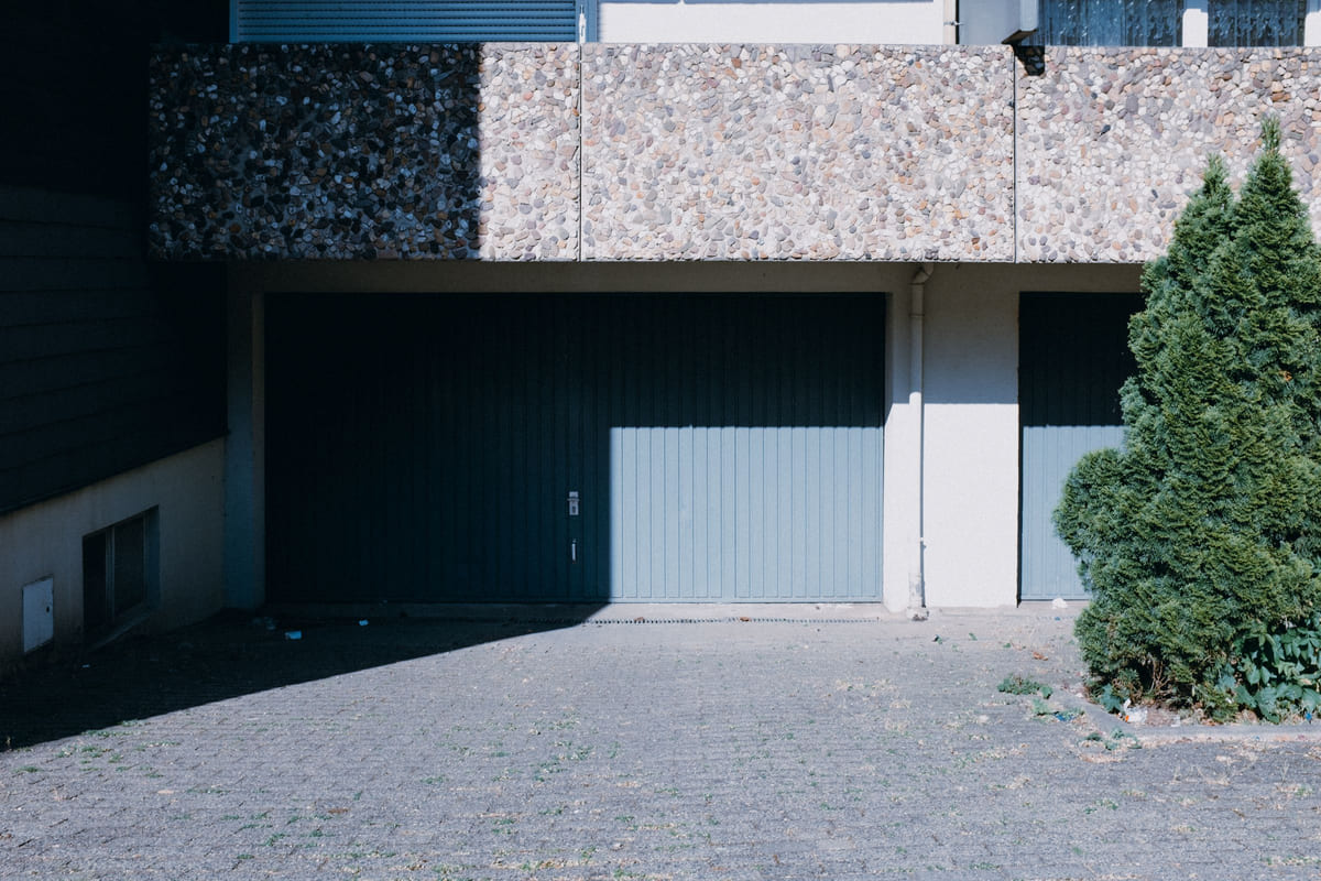 Garage doors set into the facade of a modern house beside a leafy tree.