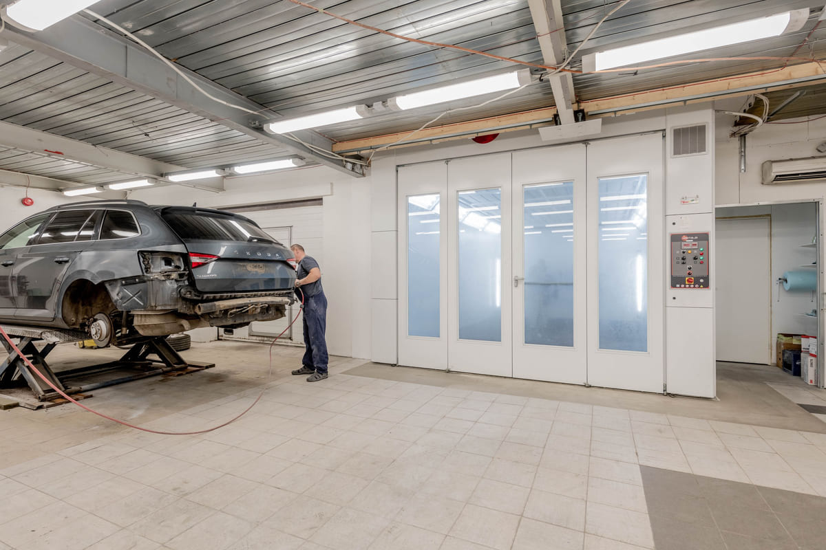 A mechanic working beside a raised car in an automotive repair workshop.