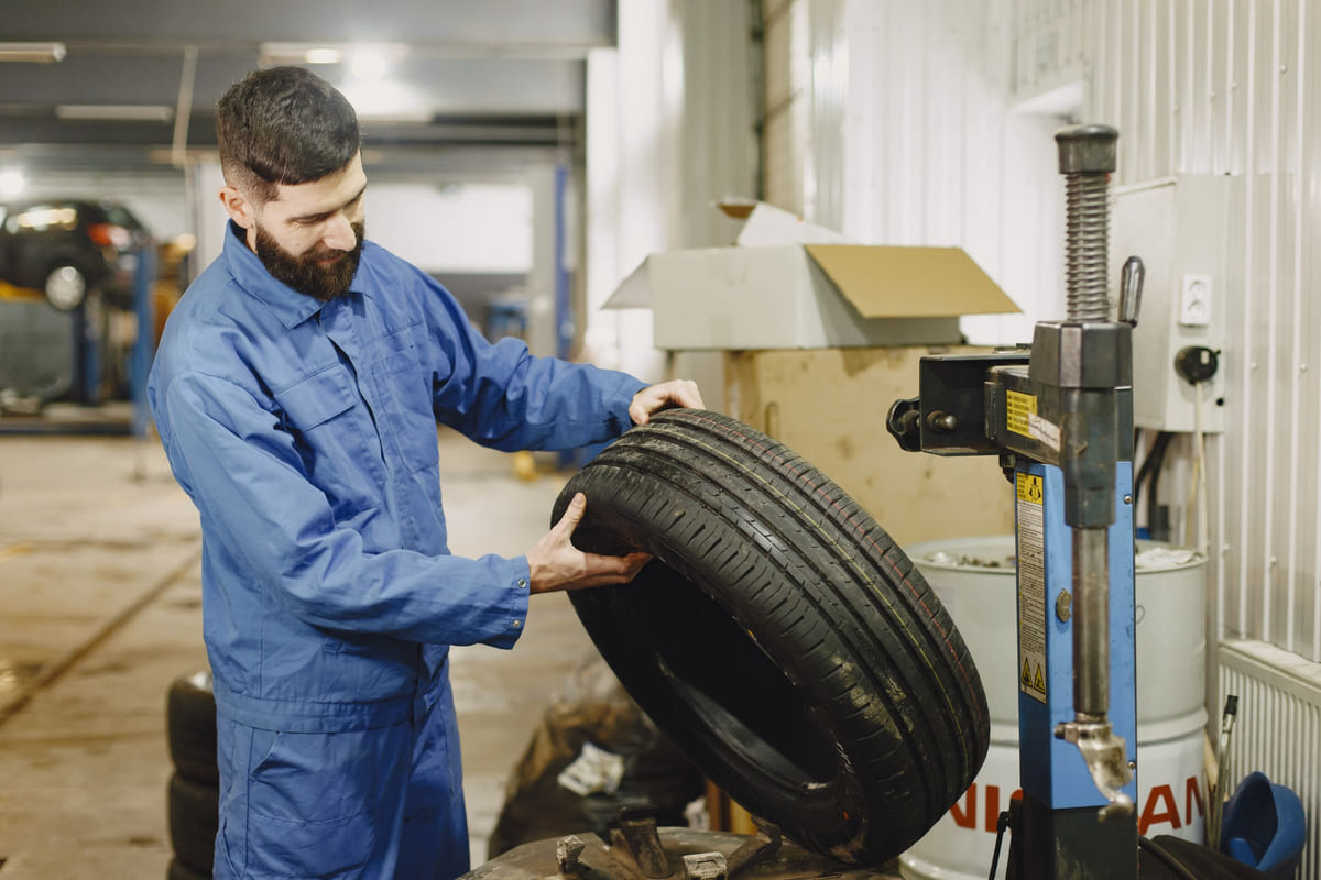 A mechanic holding a car tire beside a vehicle lift.