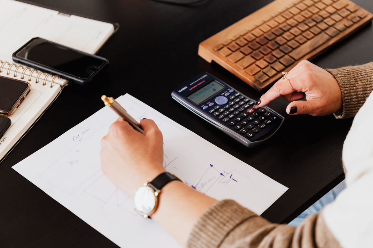 A person using a calculator while recording figures on paper.