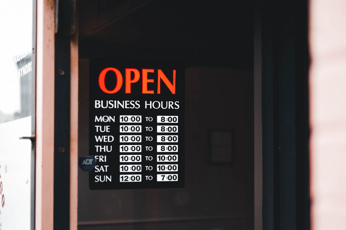 A store-window sign listing opening hours for each day of the week.
