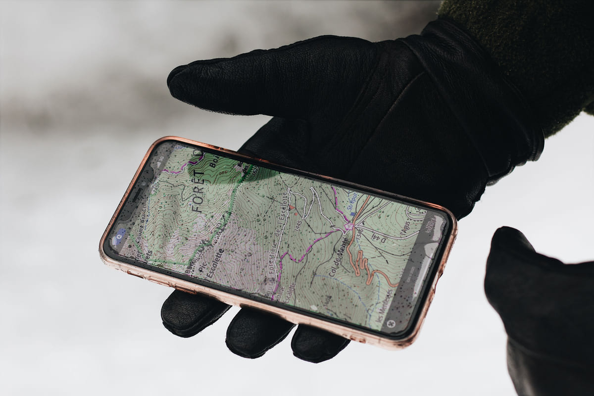 A gloved hand holding a smartphone with a map displayed.