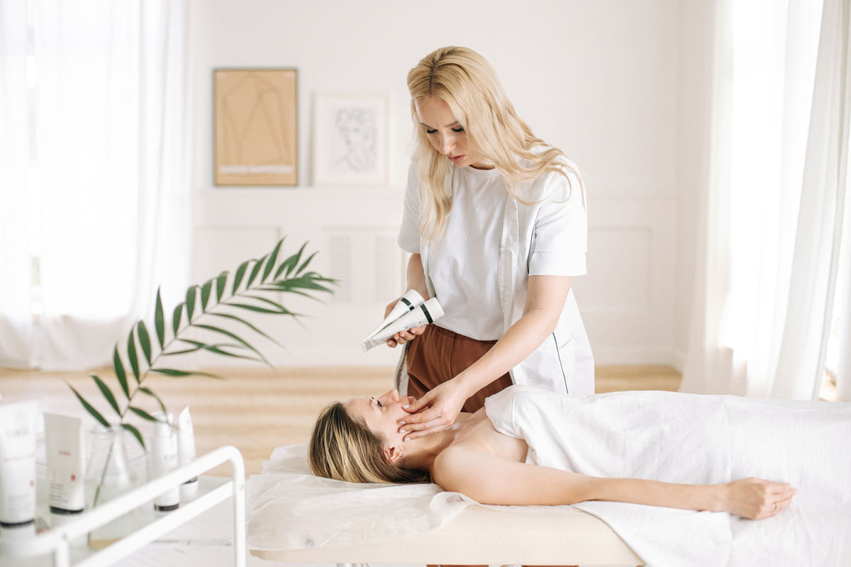A skincare specialist examining a client's face in a bright treatment room.