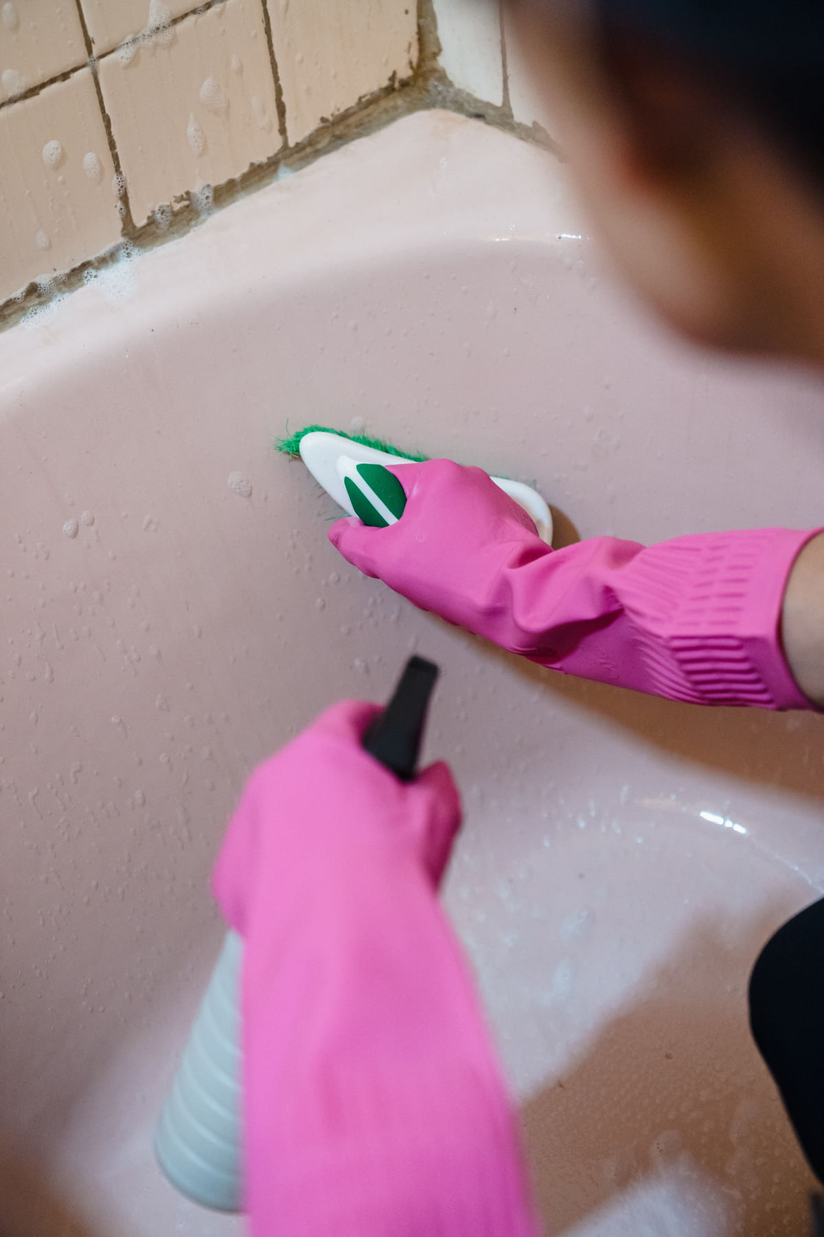 A person wearing gloves scrubbing the inside of a bathtub.