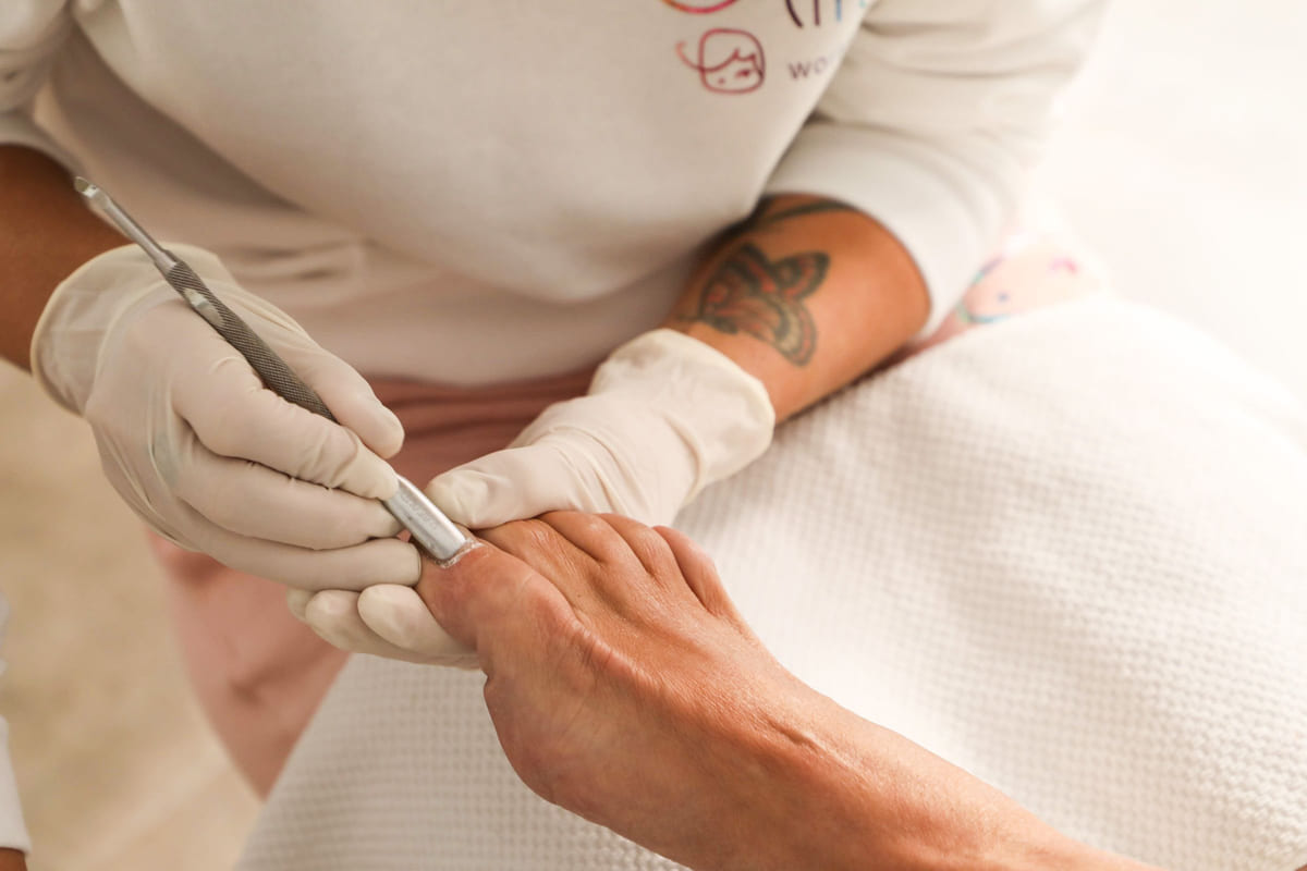A gloved nail technician using a manicure tool on a client's nails.