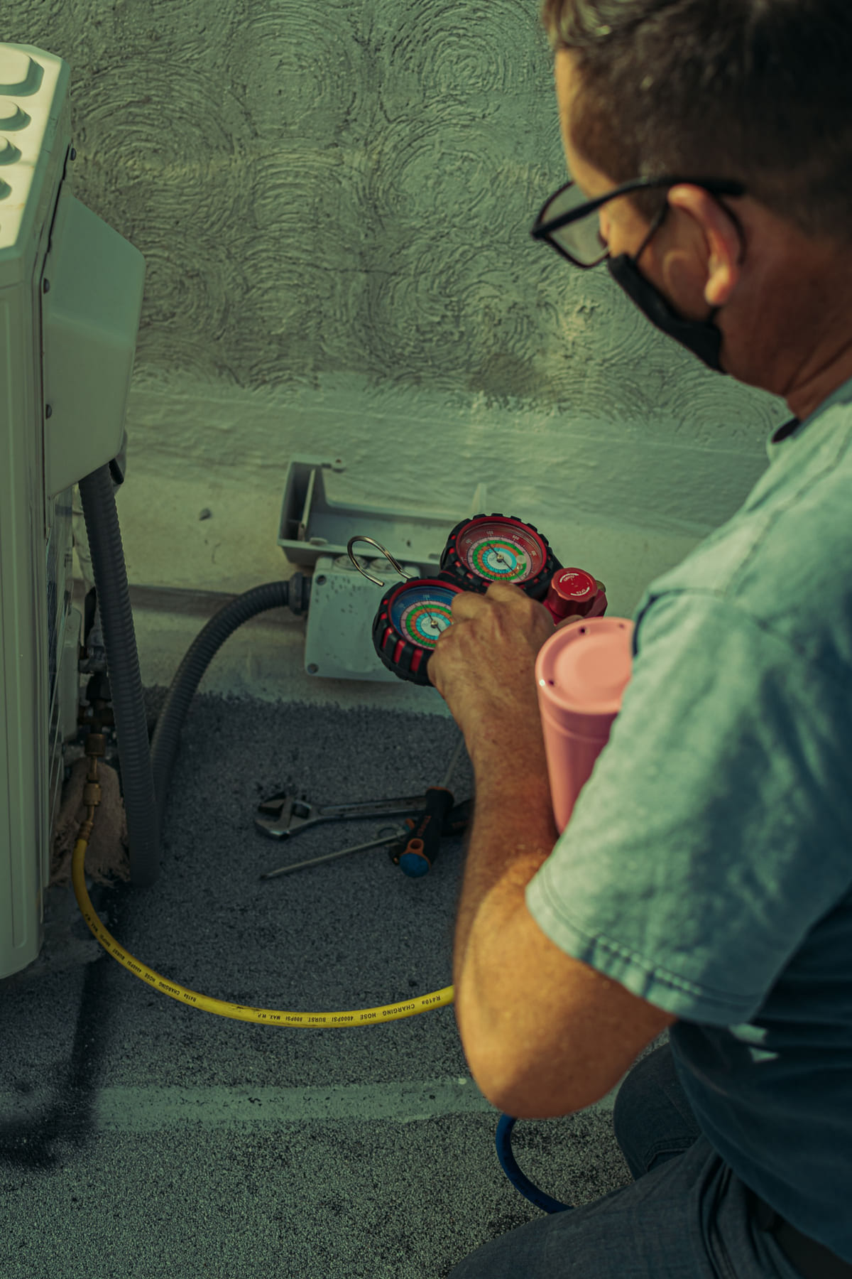 An HVAC technician working with gauges beside cooling equipment.