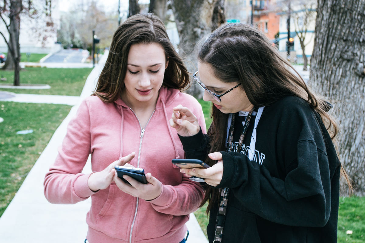 Two people checking smartphones together outdoors.