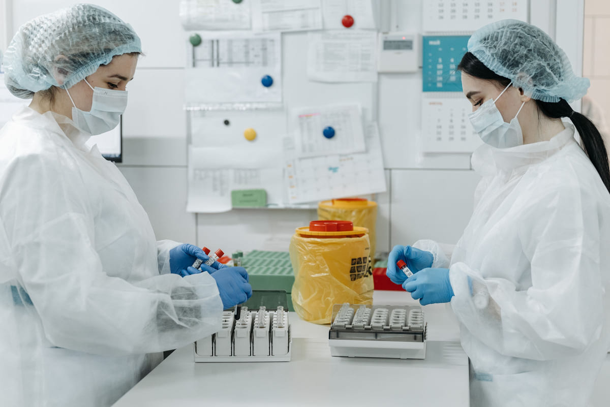 Two laboratory workers handling sample tubes at a clean bench.