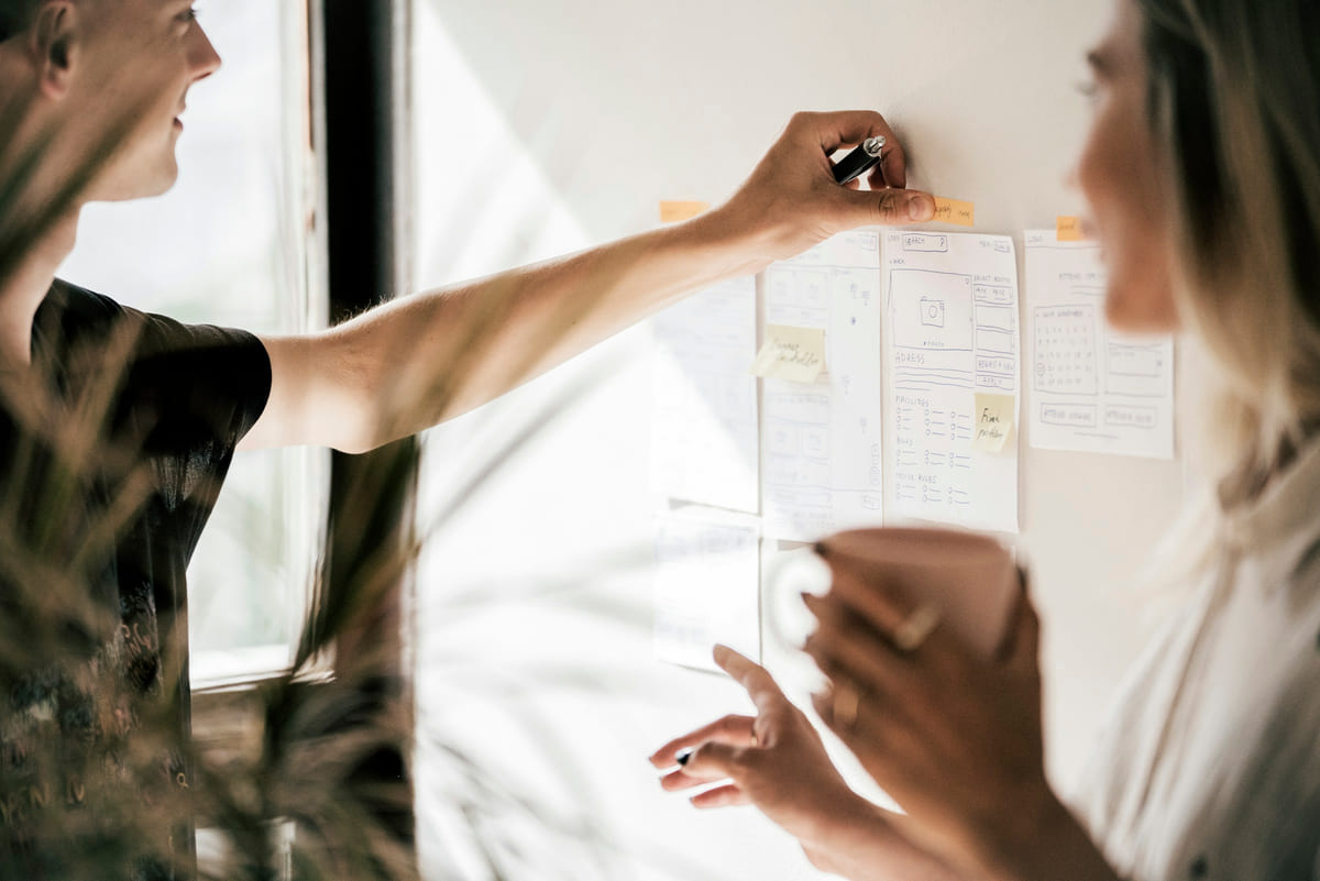 Two people discussing paper website wireframes on a wall.