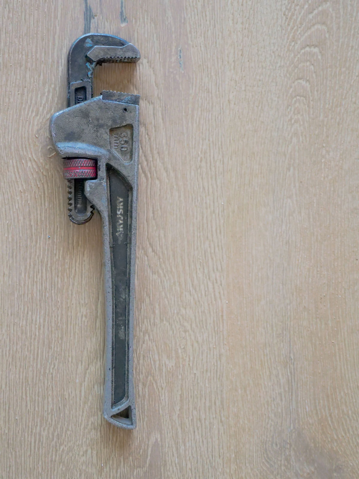A metal pipe wrench resting against a wooden surface.