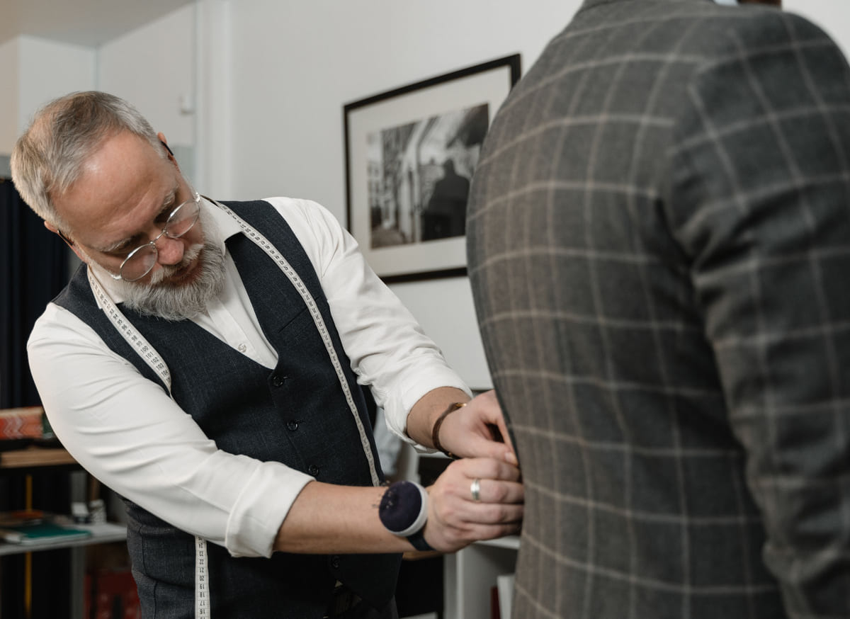 A tailor adjusting a client's jacket during a fitting.