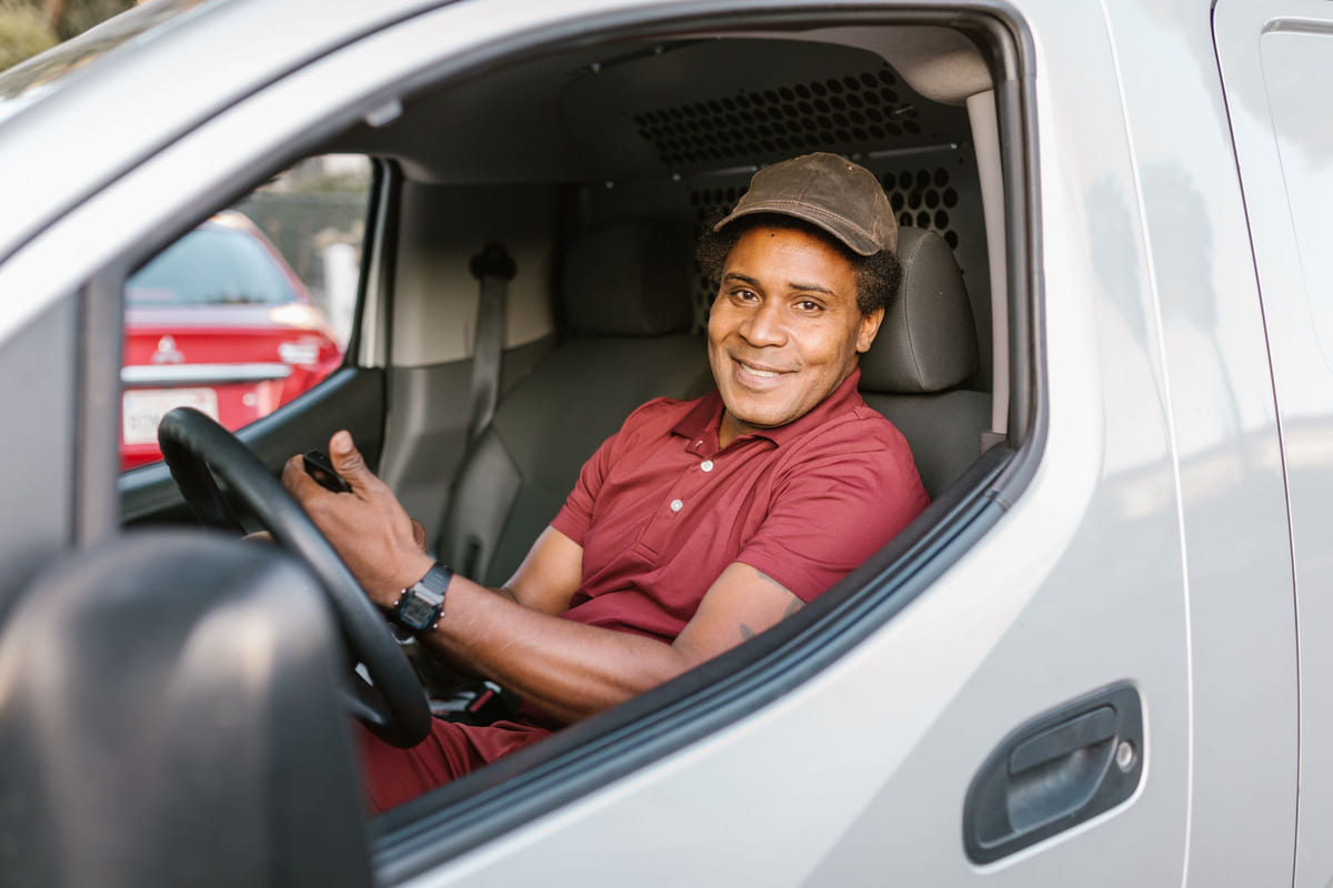 A delivery driver holding a smartphone while seated in a parked van.