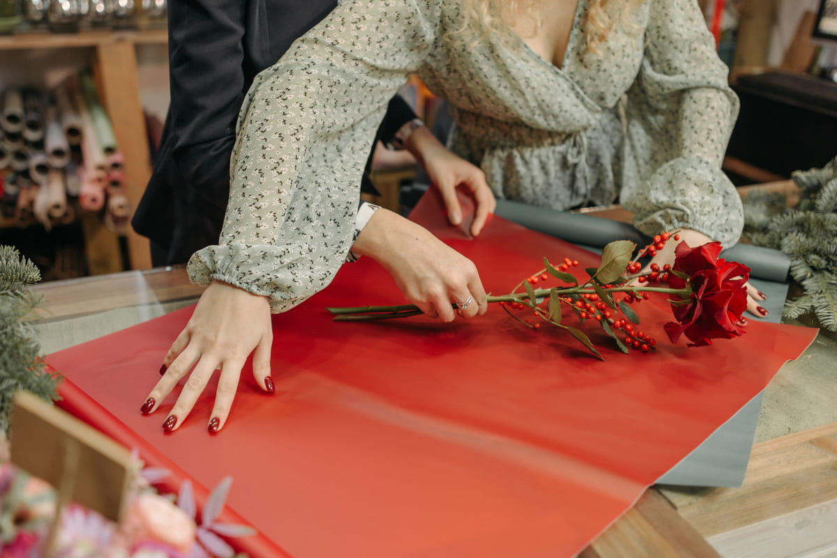 A florist wrapping a red flower in decorative paper.