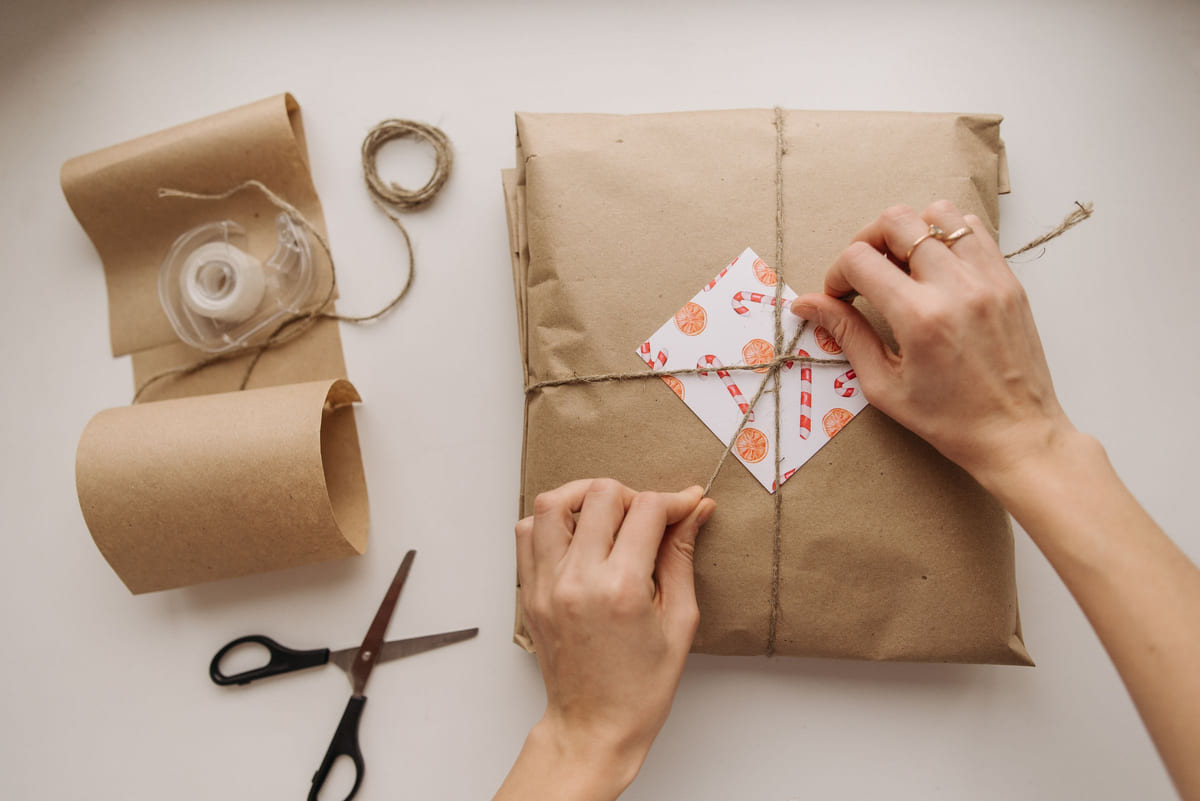Hands tying string around a parcel wrapped in brown paper.