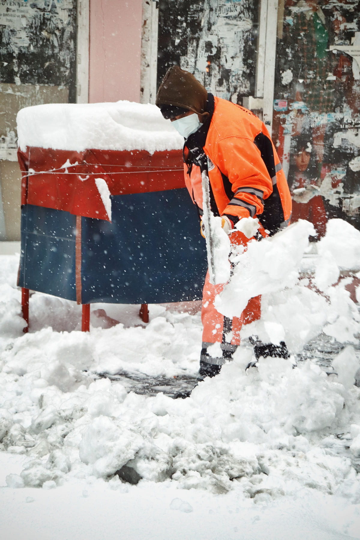 A worker shoveling snow from a sidewalk.