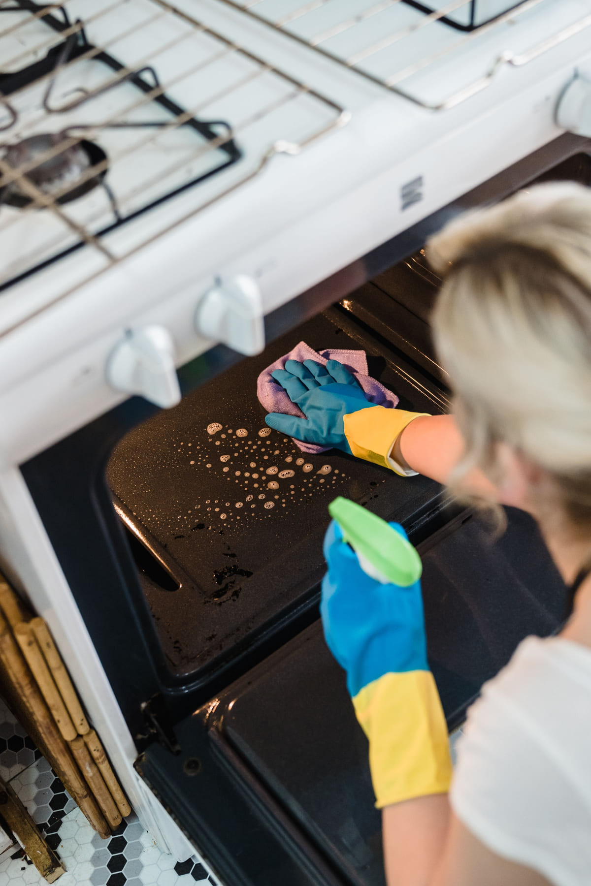 A cleaner using a sponge and spray bottle on an open oven.