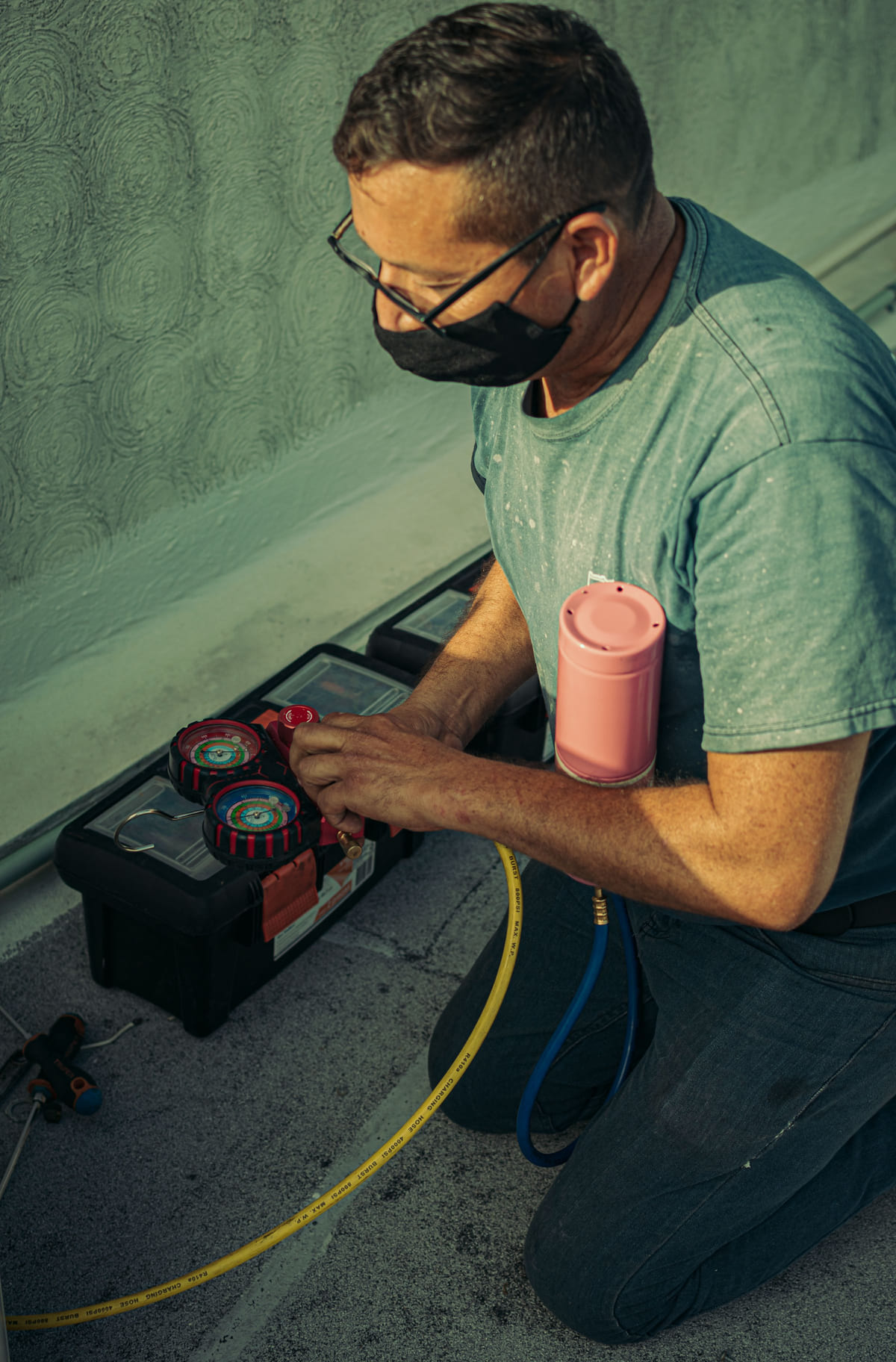 A technician servicing air-conditioning equipment with gauges and tools.