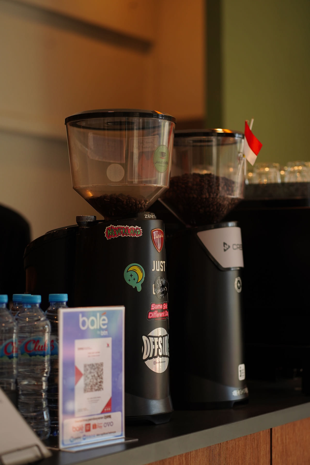 A printed QR-code card beside coffee grinders on a café counter.