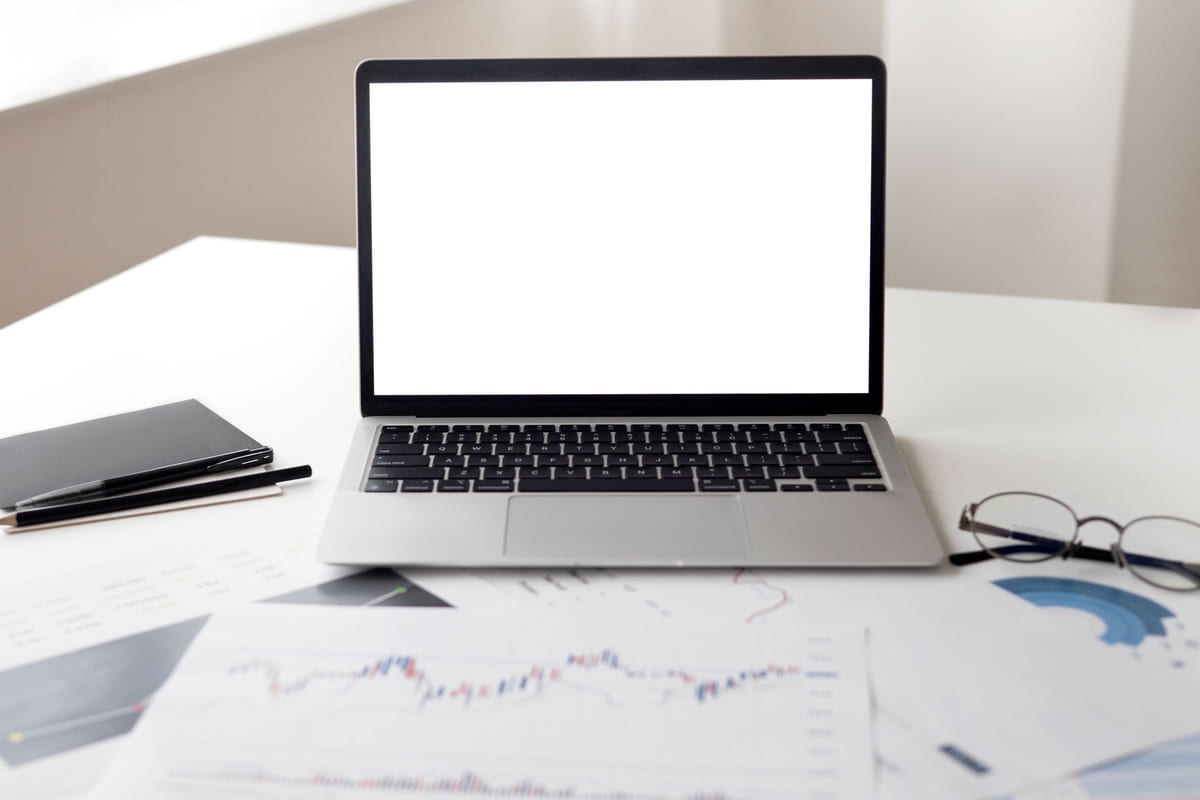 A laptop, charts and office stationery arranged on a bright desk.