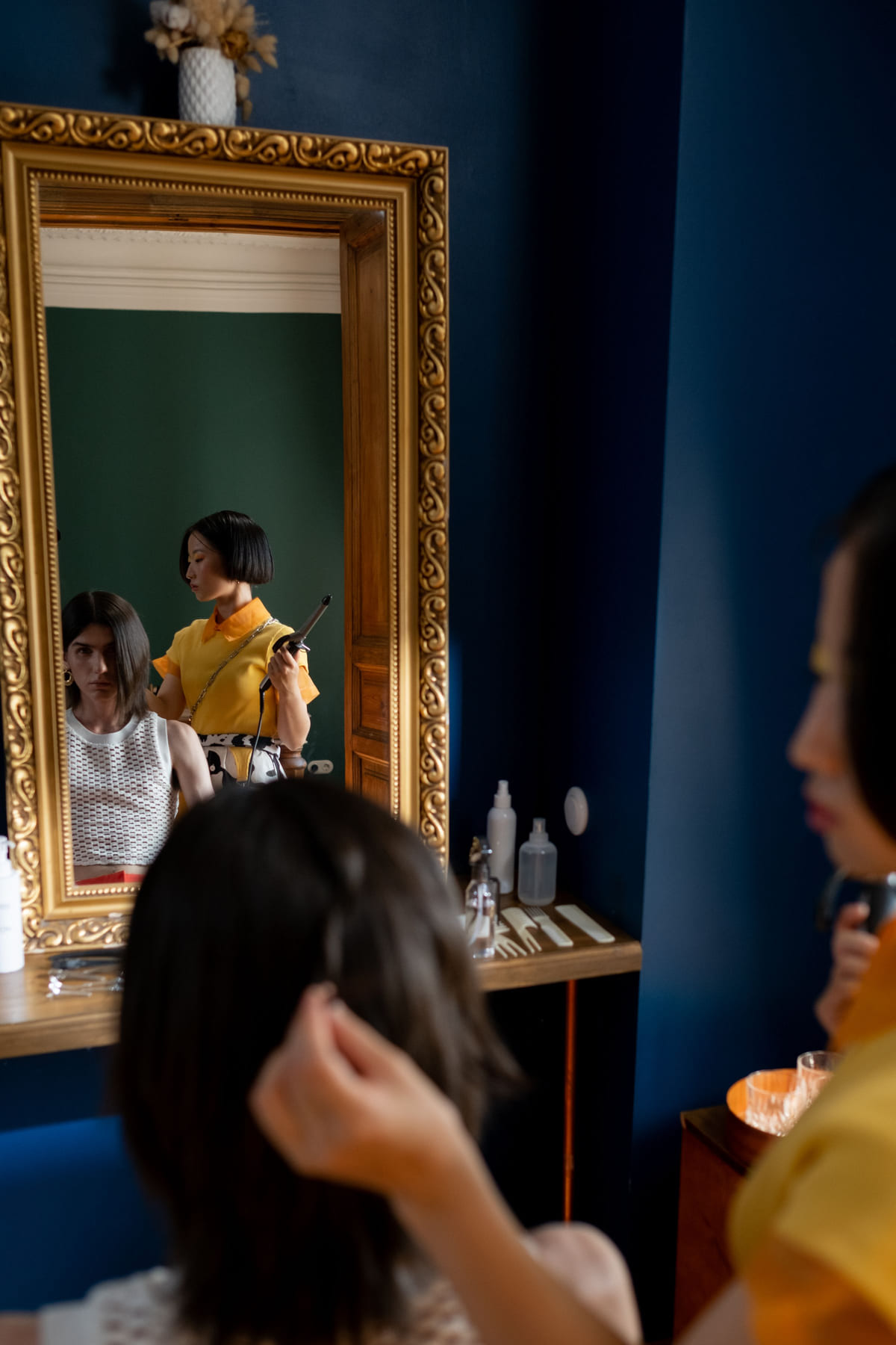 A stylist working on a client's hair beside a salon mirror.
