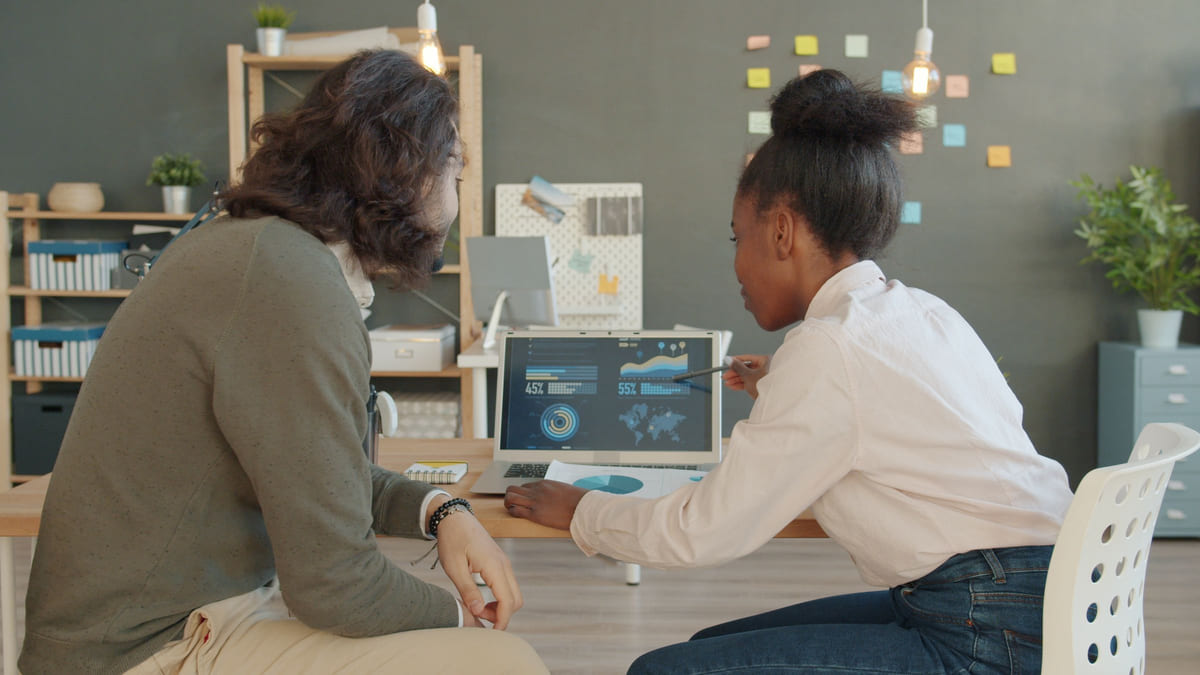 Two colleagues reviewing charts on a laptop in a bright office.