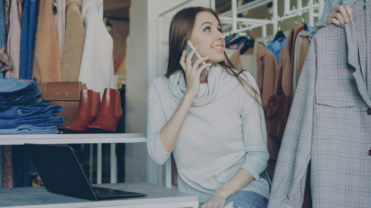 A boutique owner talking on the phone beside her open laptop.