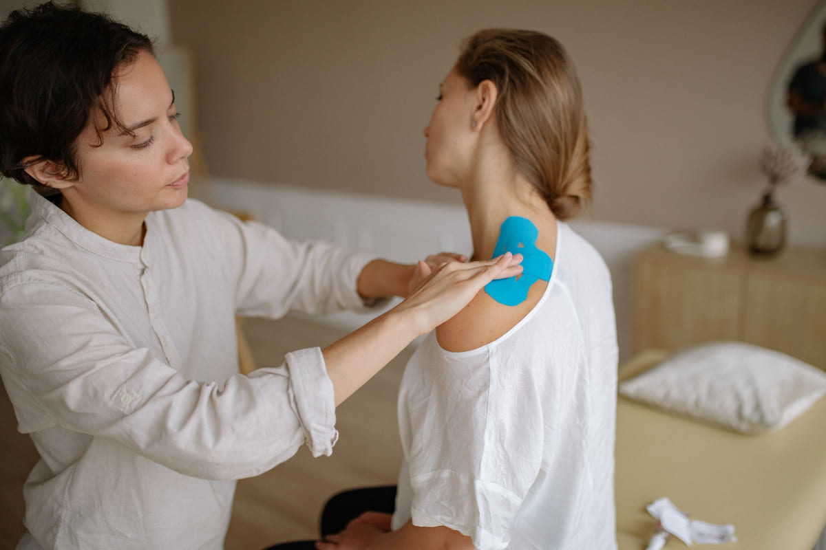 A practitioner applying therapeutic tape to a client's upper back and shoulder.