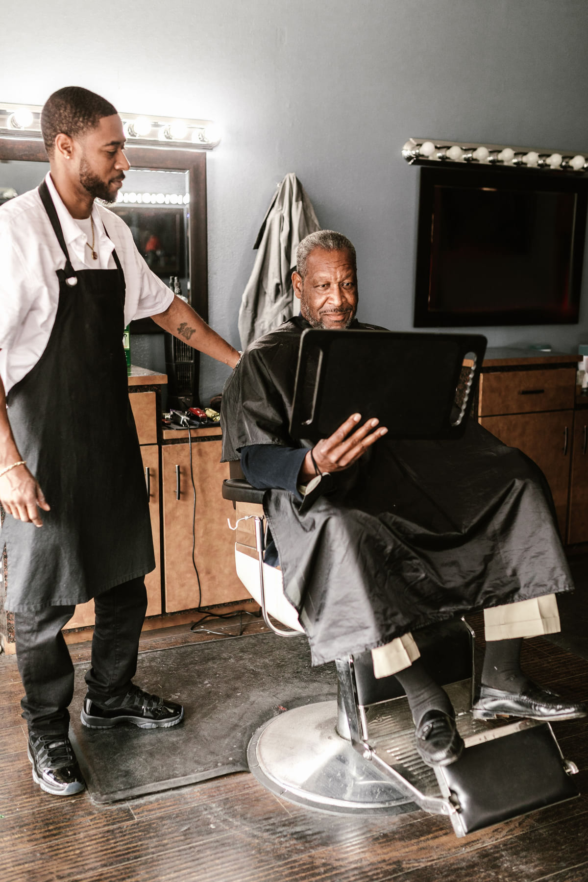 A barber assisting a seated customer at the end of a service.