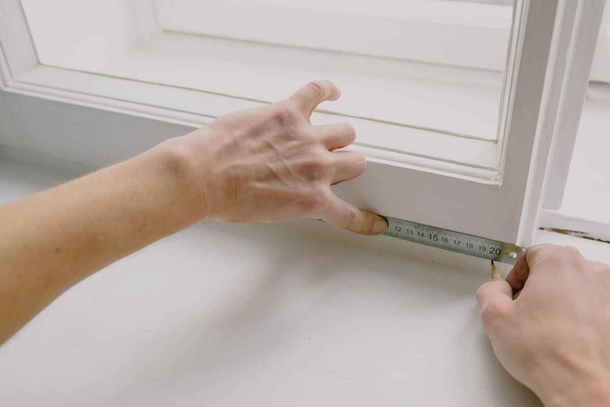 Hands measuring the inside of a window frame.